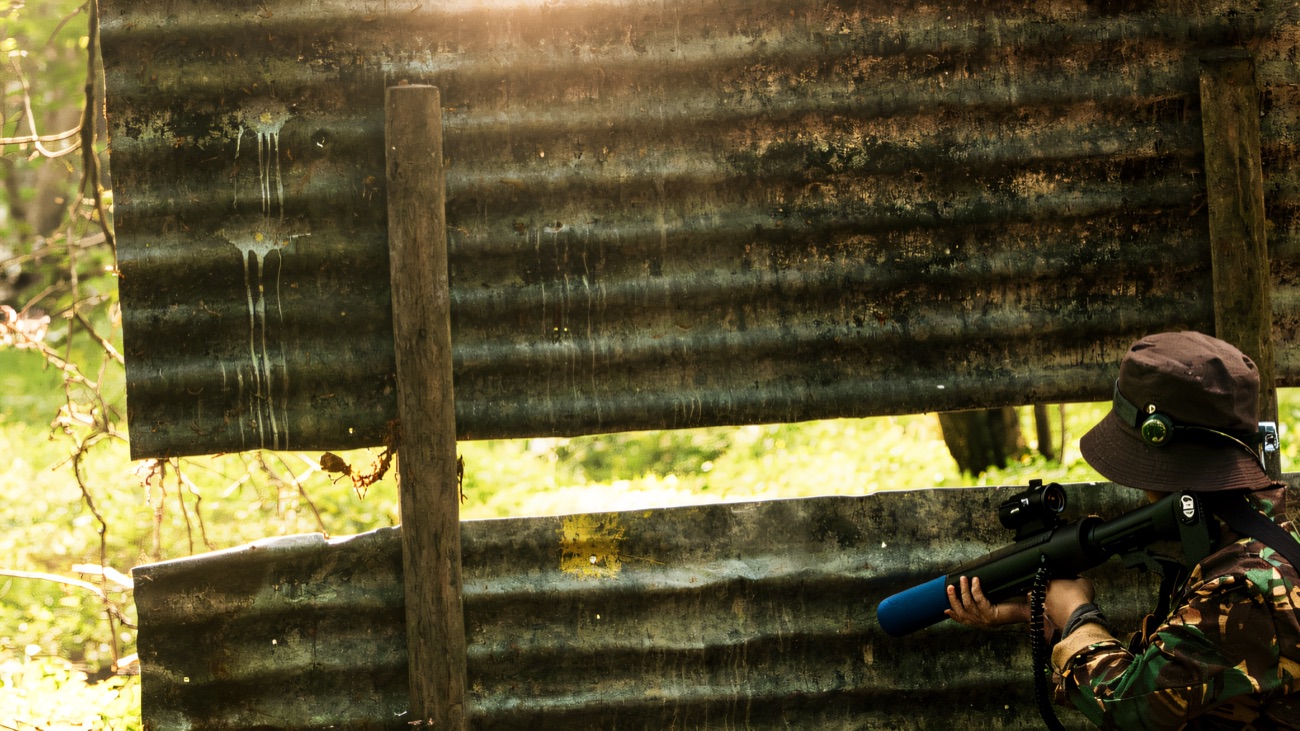 A player taking cover behind a corrugated tin barricade in the trees
