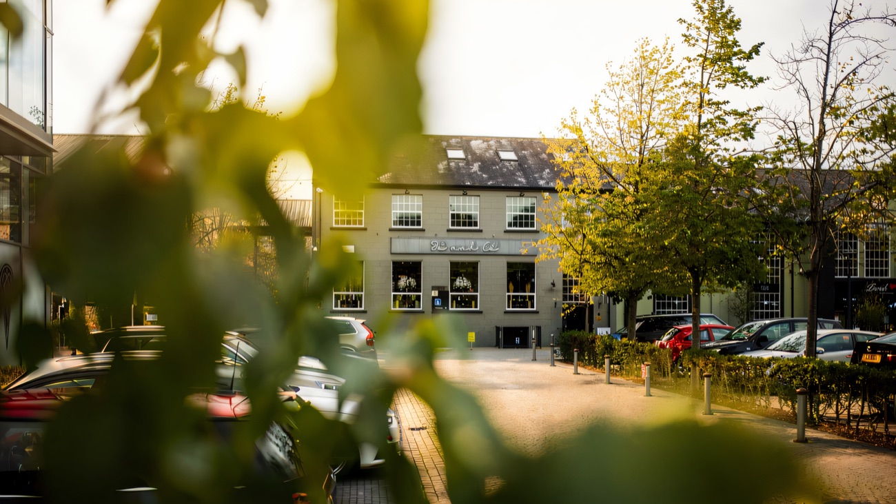 The two-storey grey mill building at The Linen Green seen across the courtyard through the trees