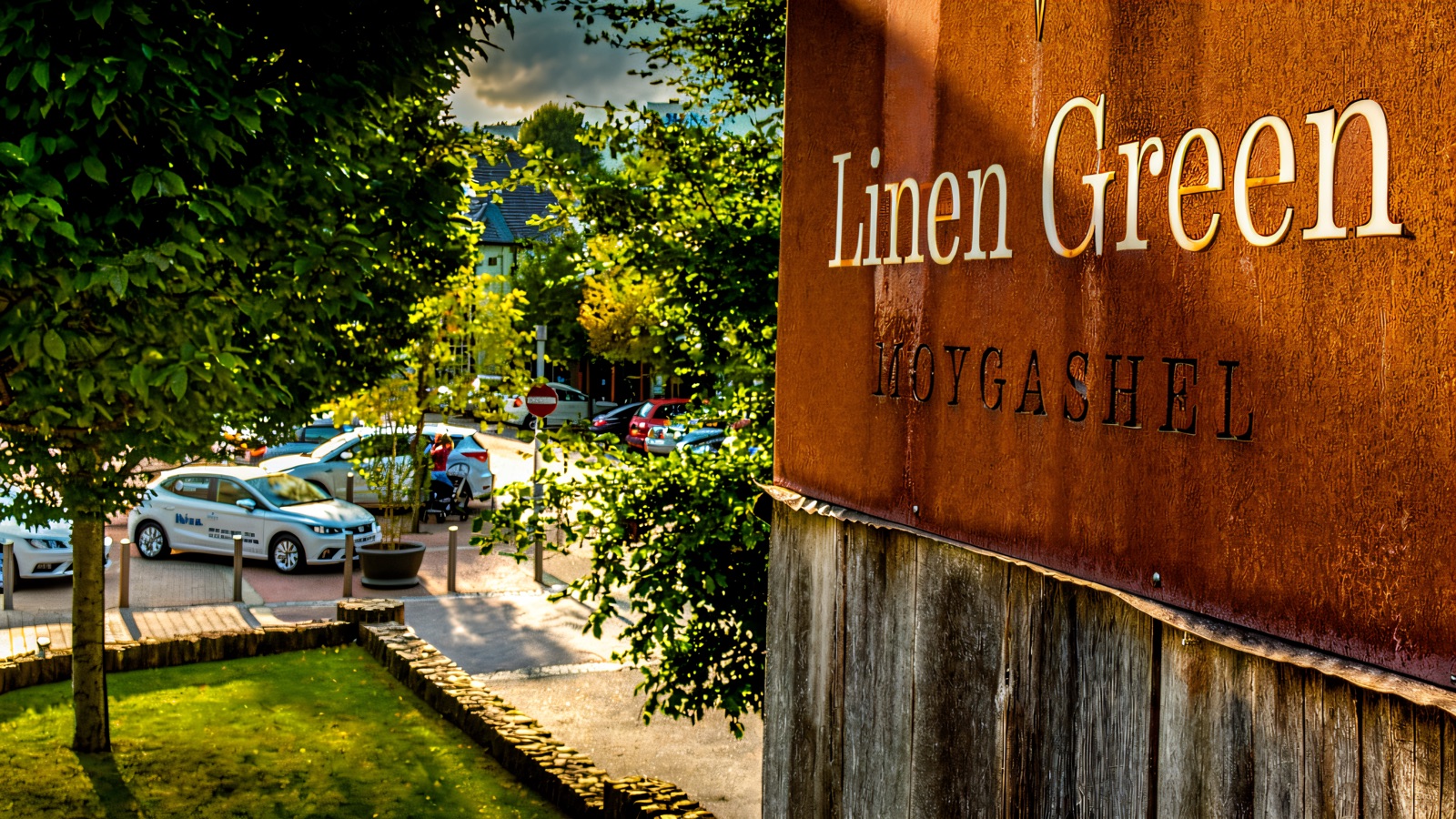 The weathered-timber Linen Green Moygashel entrance sign, with the shopping village and car park behind