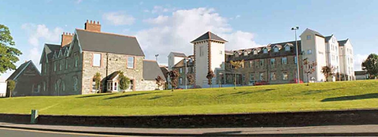 A wide view of the restored grey-stone workhouse building set behind a green bank, with its distinctive tower and later library wings