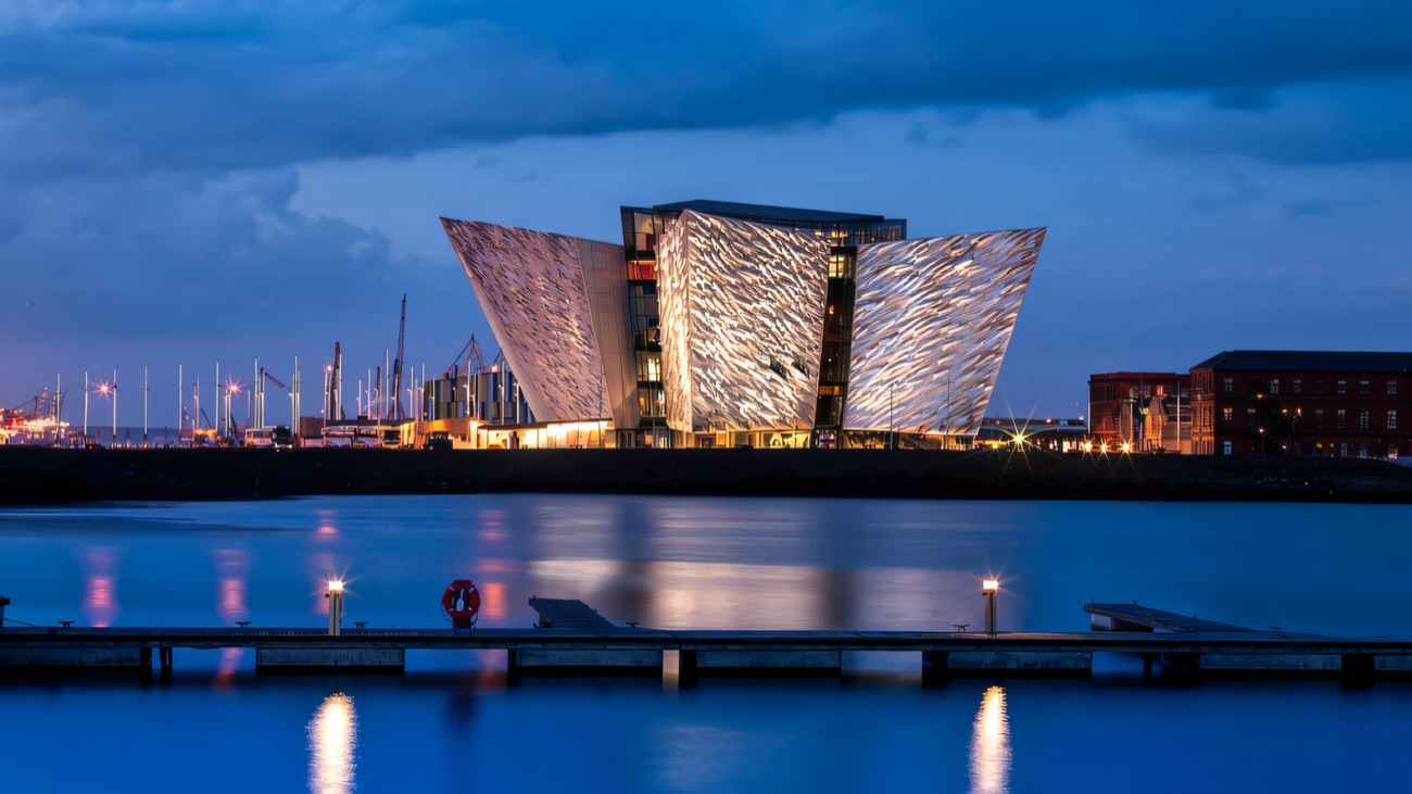 The Titanic Belfast building lit up at dusk, reflected in the water