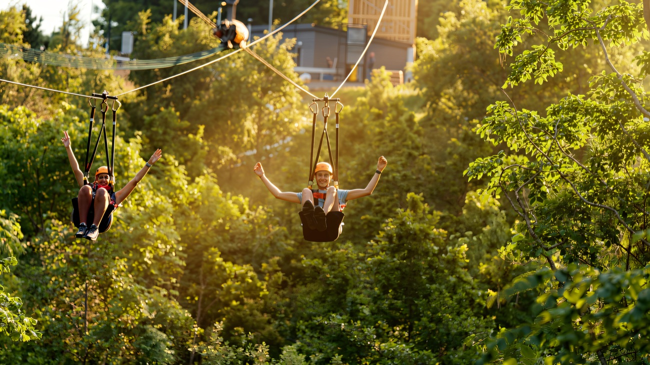 Two flyers whooping down the parallel ziplines over the treetops
