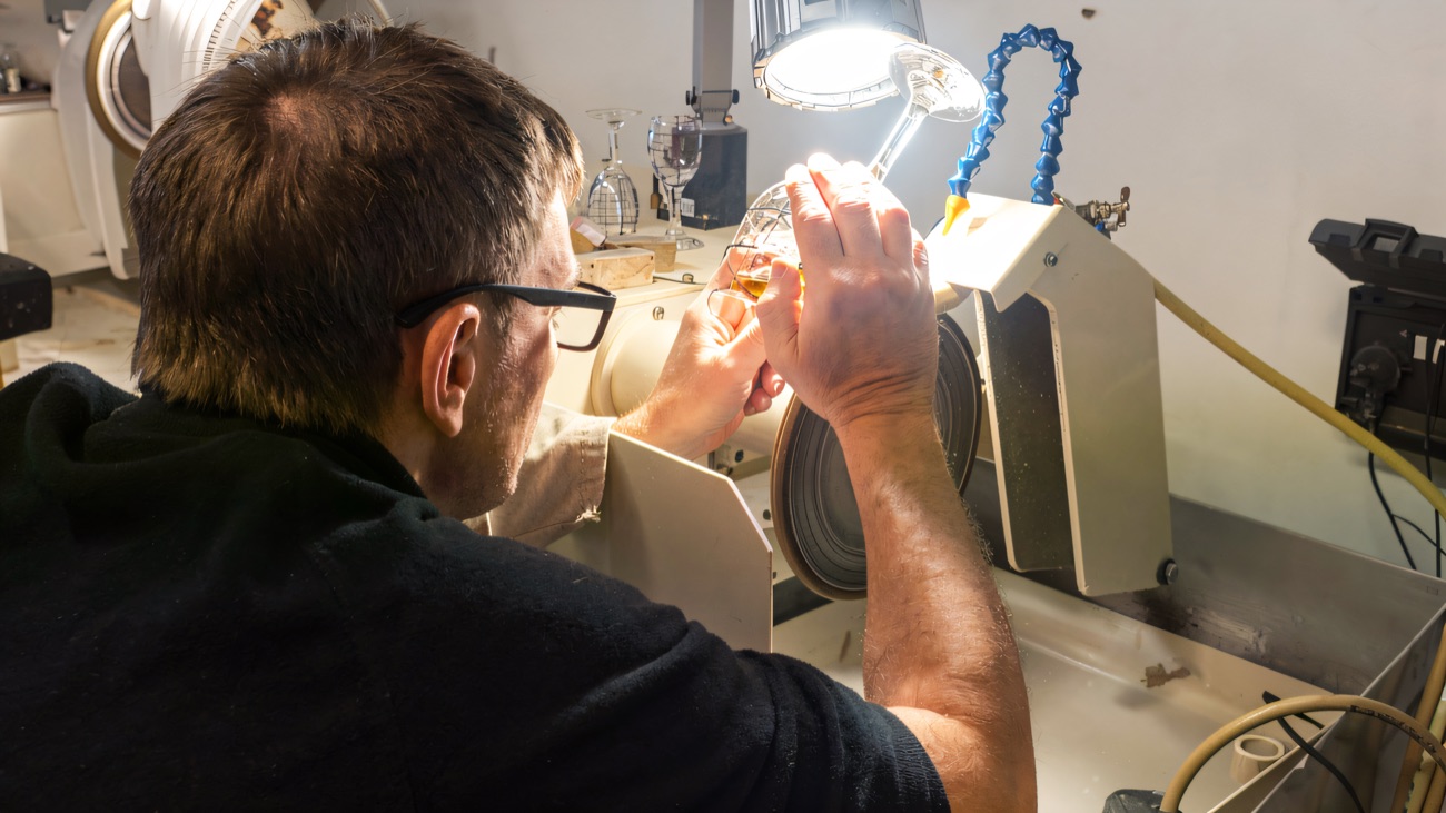 A craftsperson at the cutting wheel, shaping the decoration on a piece of hand-cut glass.