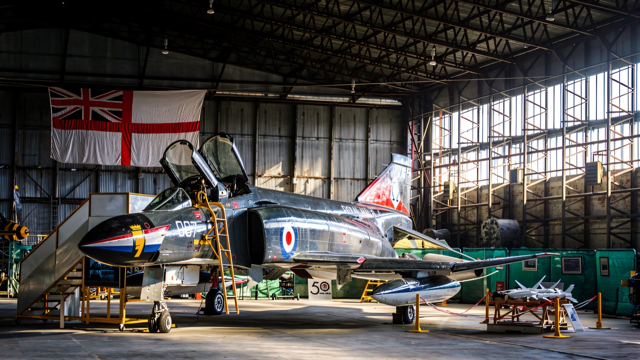 A Royal Navy Phantom parked inside the hangar beneath a hanging White Ensign