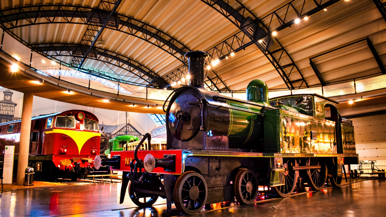 Steam locomotives and carriages under the arched roof of the railway gallery at the Ulster Transport Museum
