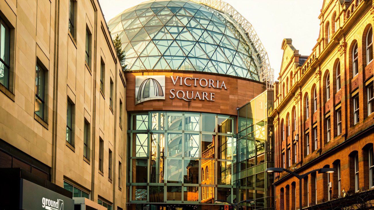 The glass dome of Victoria Square rising above the Victoria Square sign and the red-brick buildings at the entrance from the street