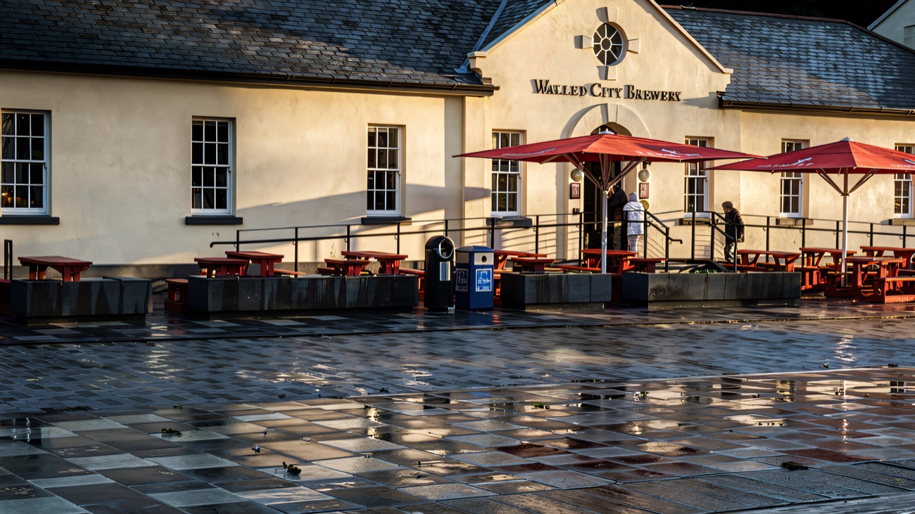 Red picnic benches and parasols on the open paved square outside the brewery on a wet day.
