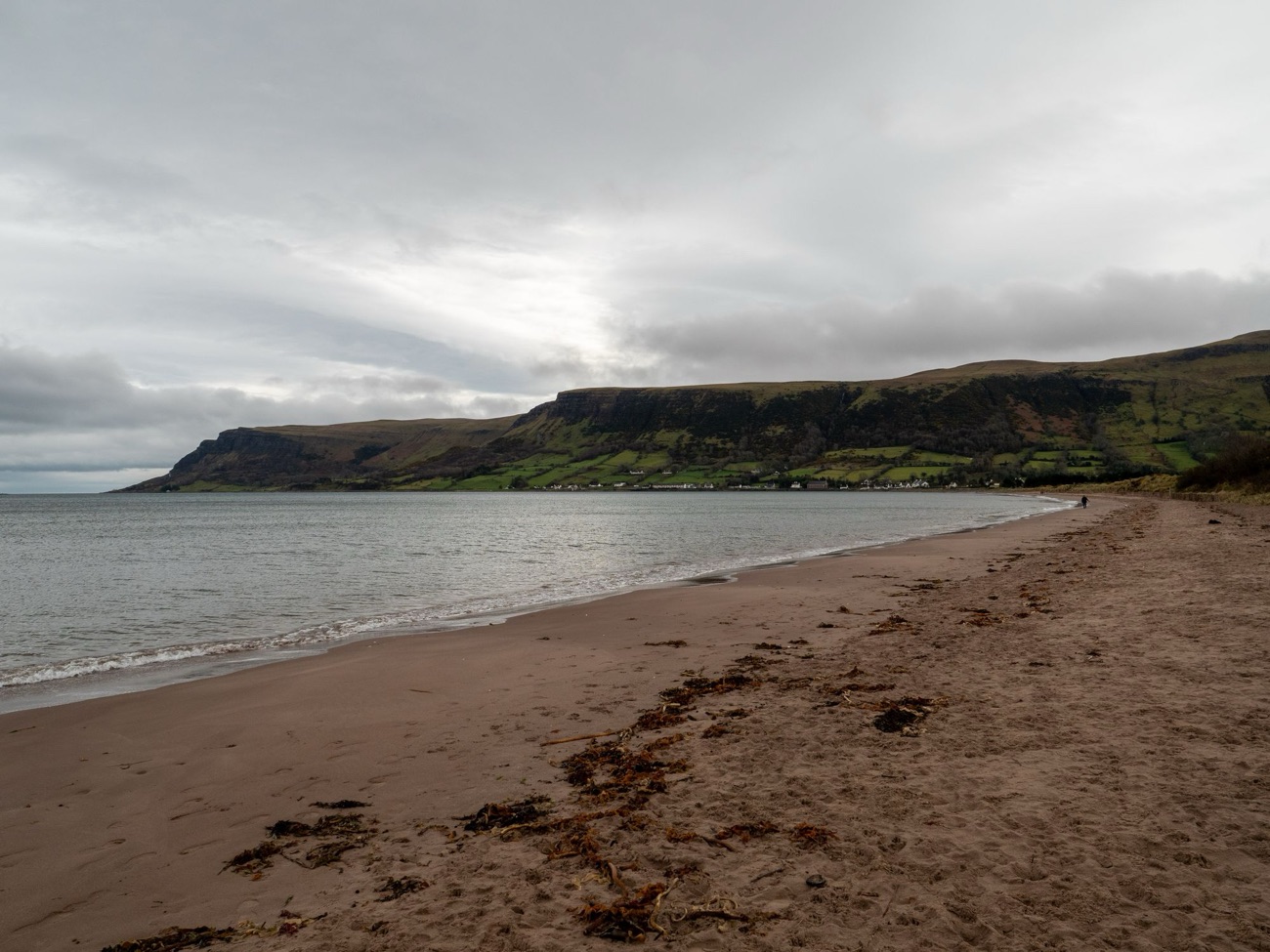 The wide sandy beach at Waterfoot backed by the dramatic table-top cliffs and green slopes of the Glens of Antrim