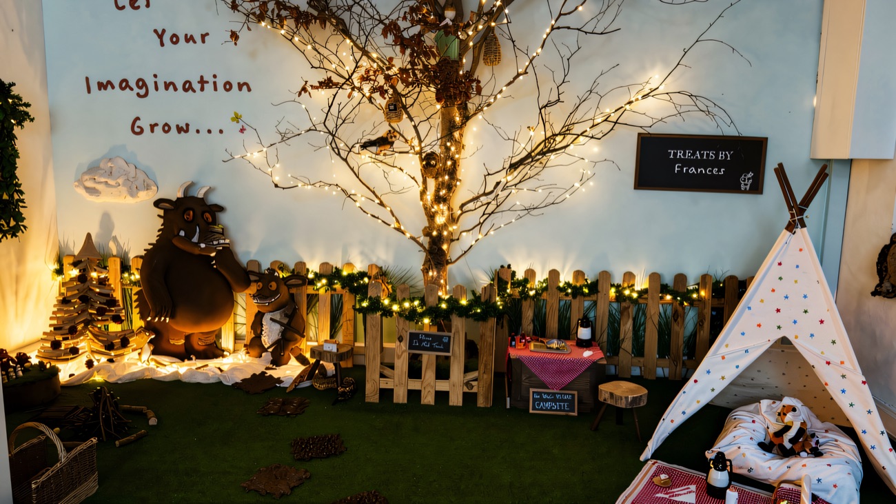 A woodland campsite play corner with a lit tree, teepee and picnic blanket