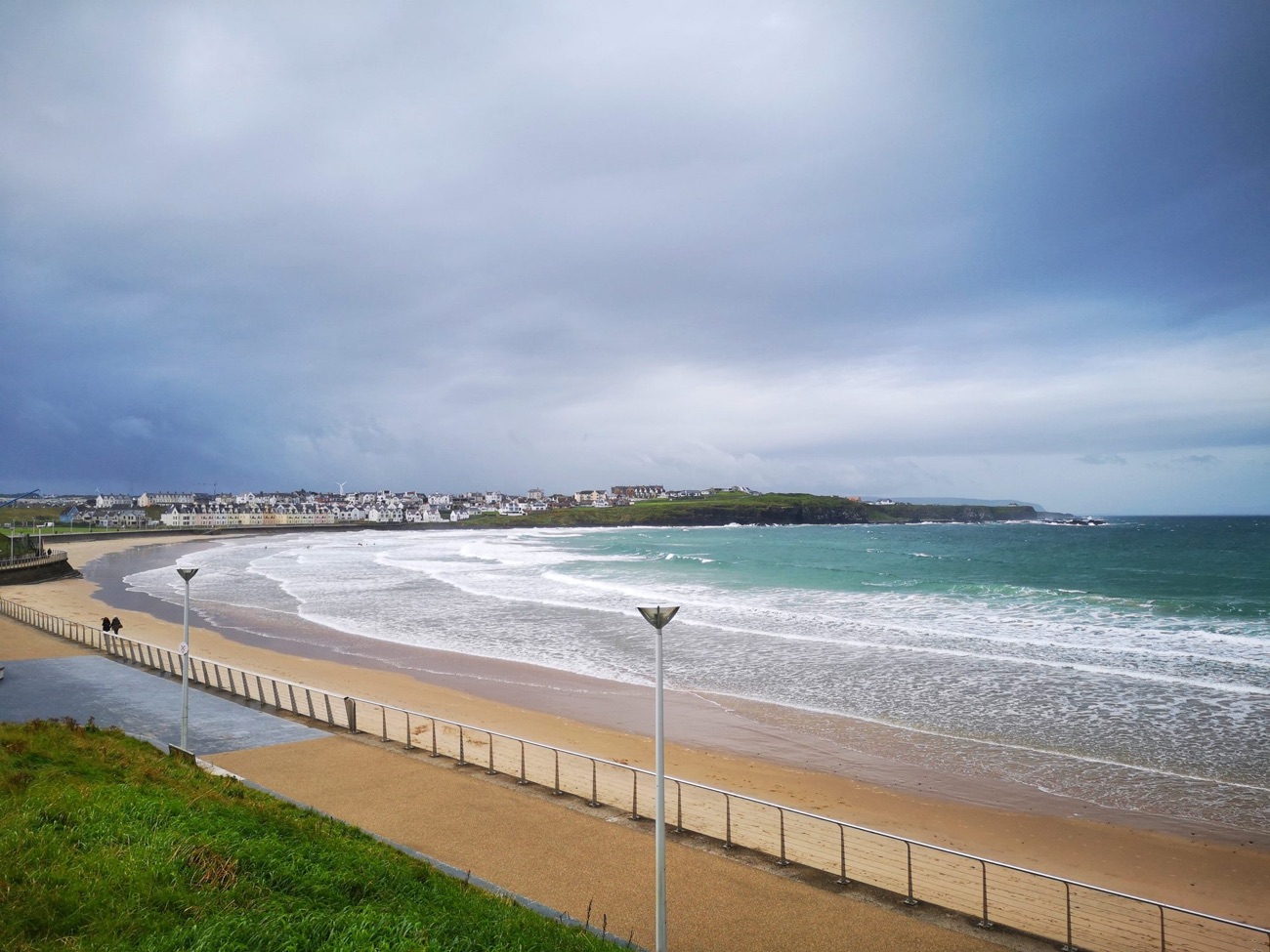 The promenade path and railing running alongside West Strand beach with the surf rolling into the bay