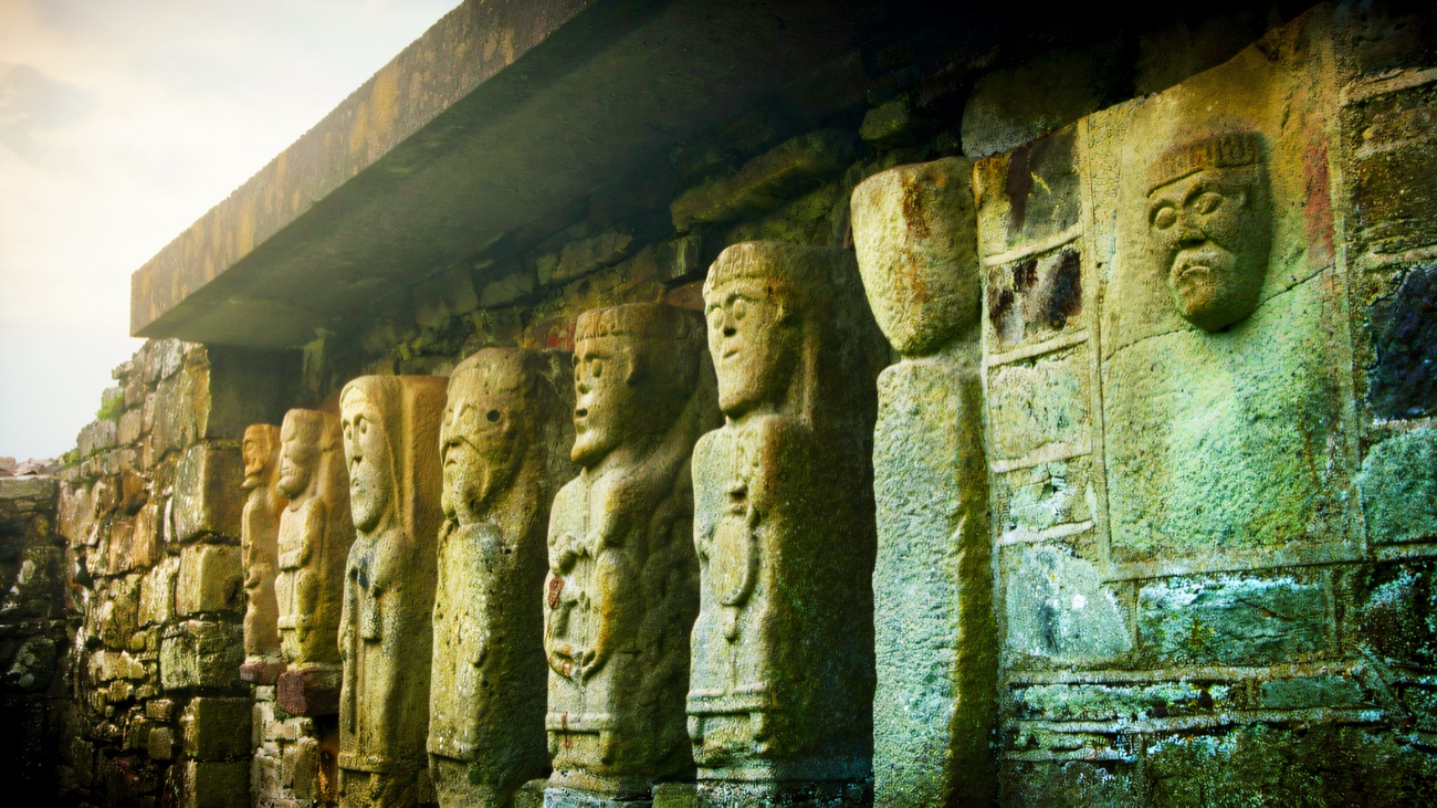 The line of stone figures along the wall, lit by a soft pink evening sky.