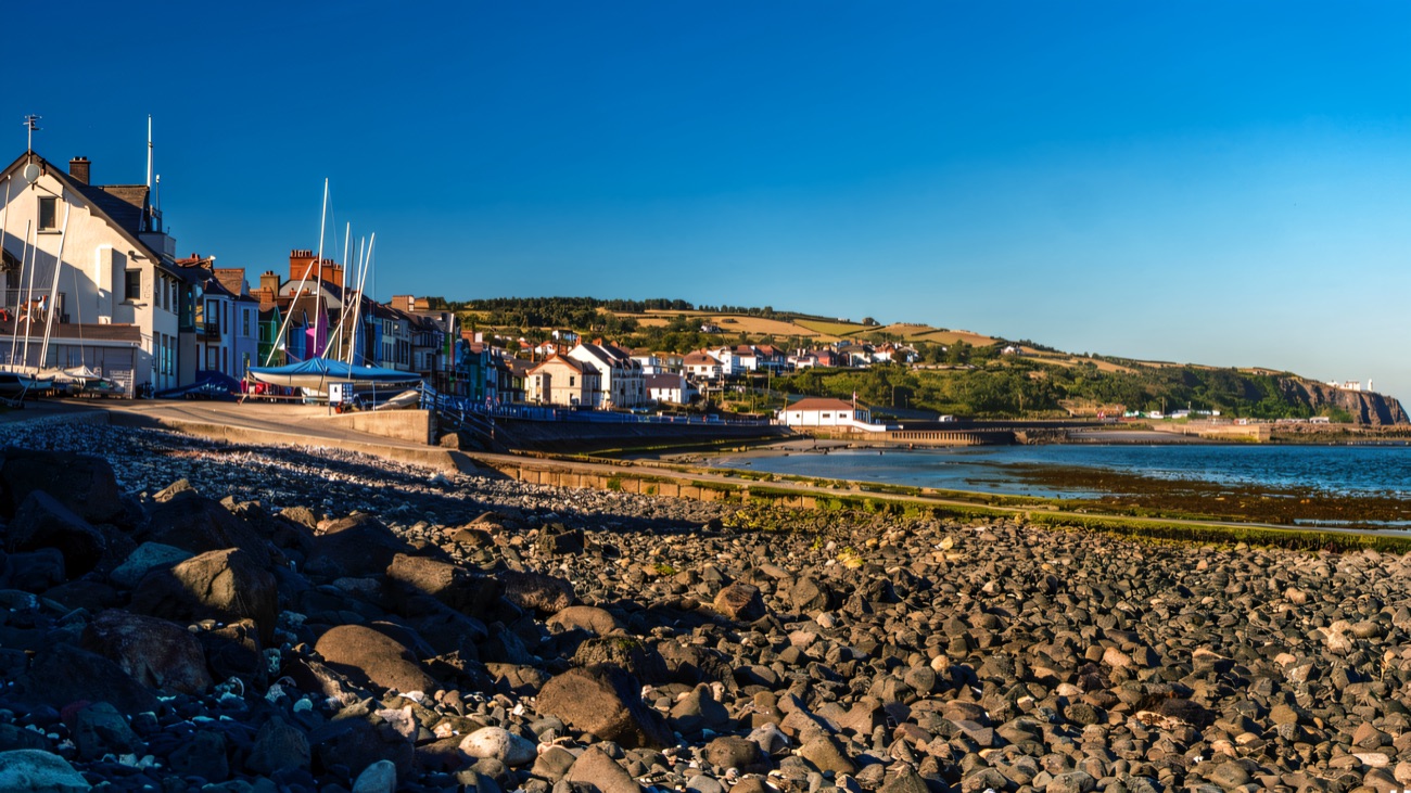 Whitehead's promenade and boat park seen across the cobble shore, with the headland beyond