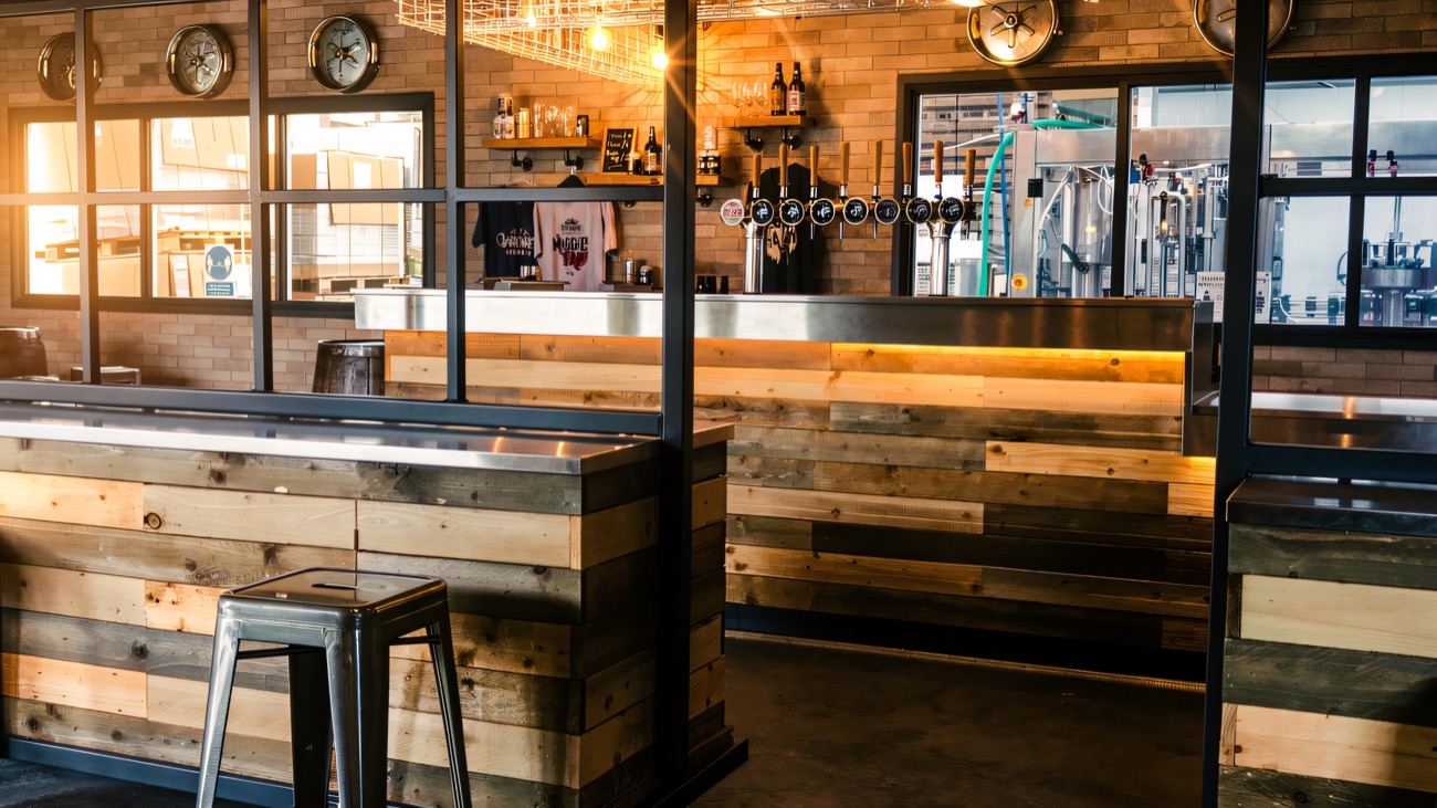 The taproom counter with keg ends on the wall and a window through to the brewing equipment.